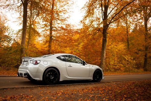 Free A sleek sports car parked on a road surrounded by vibrant autumn foliage in Denmark. Stock Photo