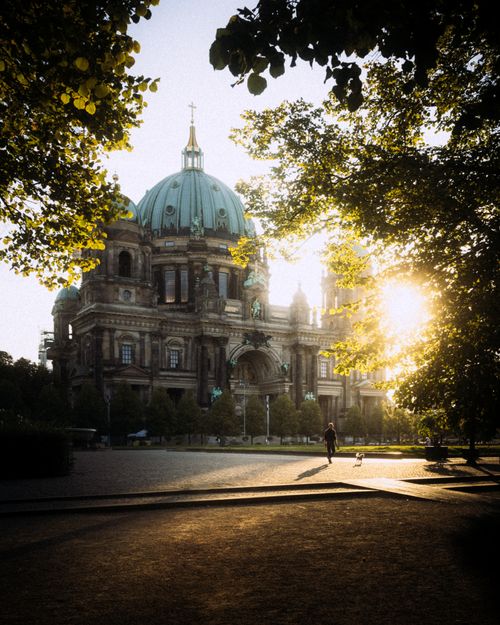 Free Scenic view of Berlin Cathedral with sunlight filtering through the trees at sunset. Stock Photo