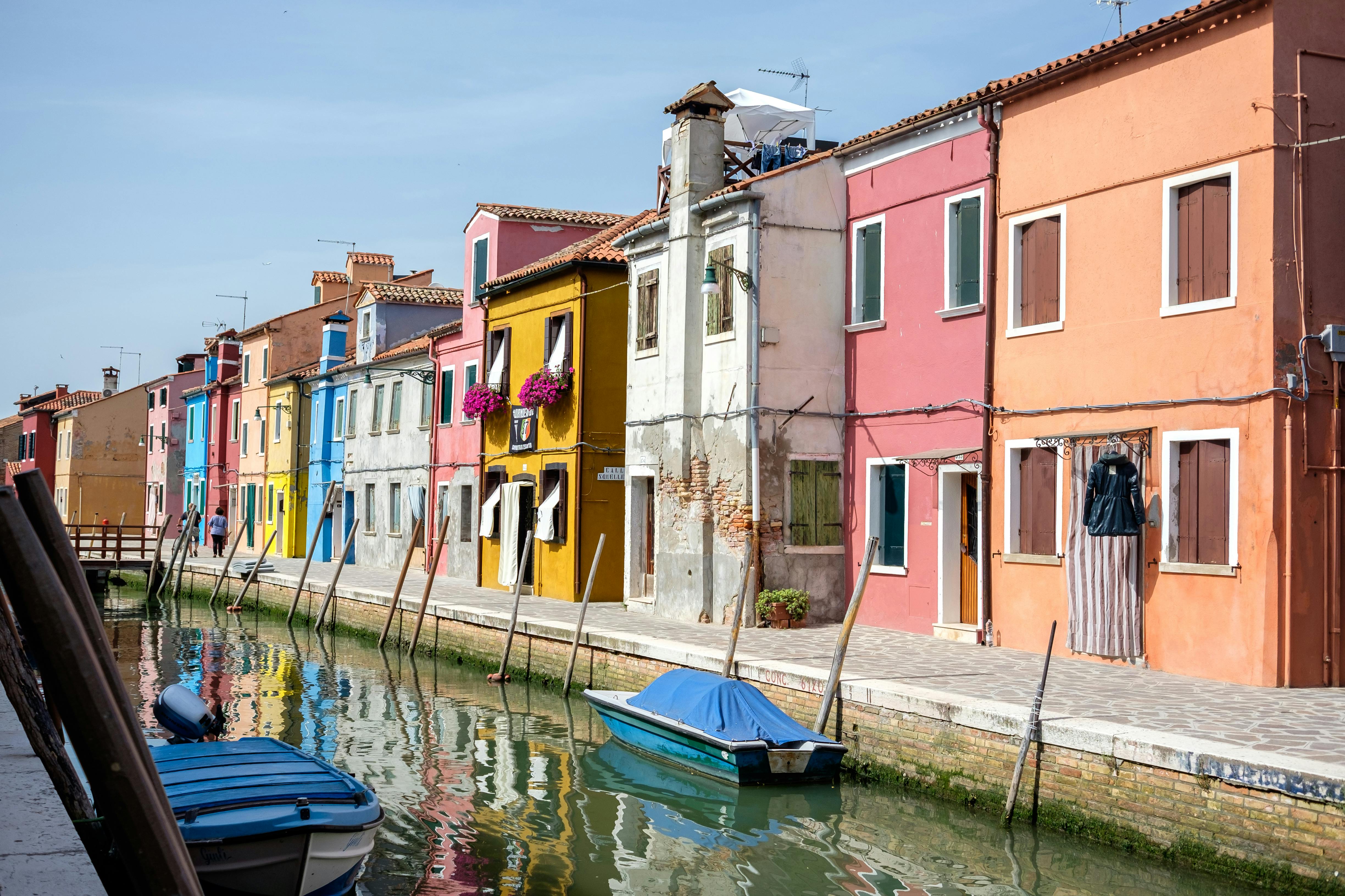 Vibrant facades along a tranquil canal in Burano, Italy, showcasing scenic charm.