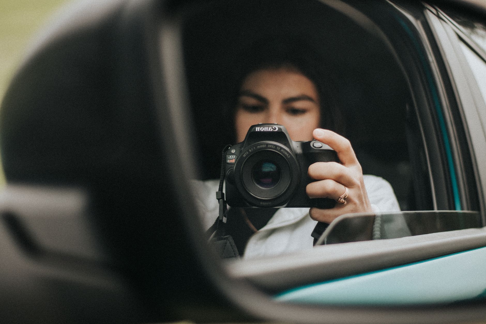 Woman taking a photo of herself in a car side mirror using a camera.