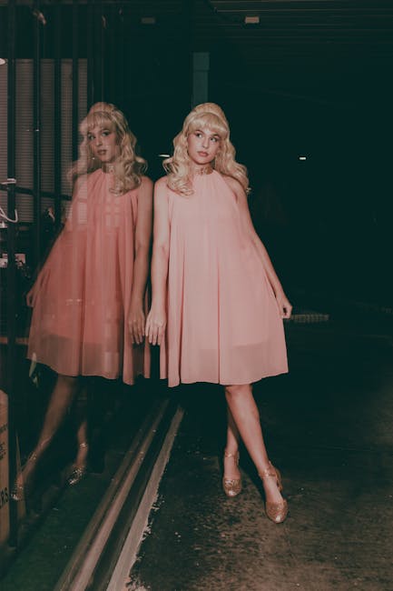 Blonde woman in a pink dress leans against a window