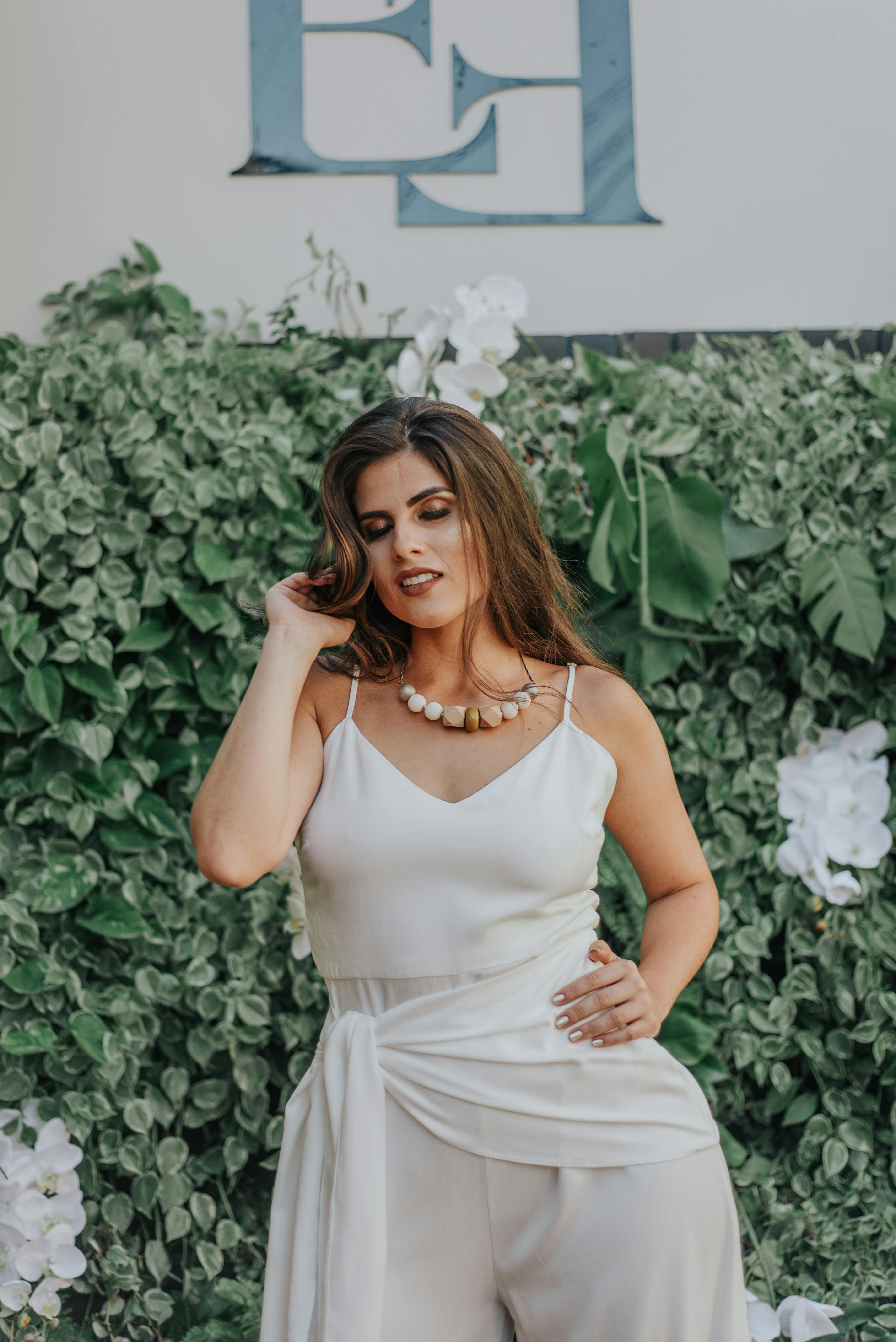 一位身着白衣的精致女子，在葱郁的绿意背景前优雅摆姿，尽显时尚气息