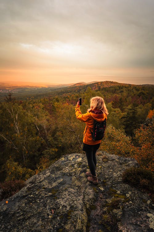Woman Standing on Rocks over Forest and Taking Pictures