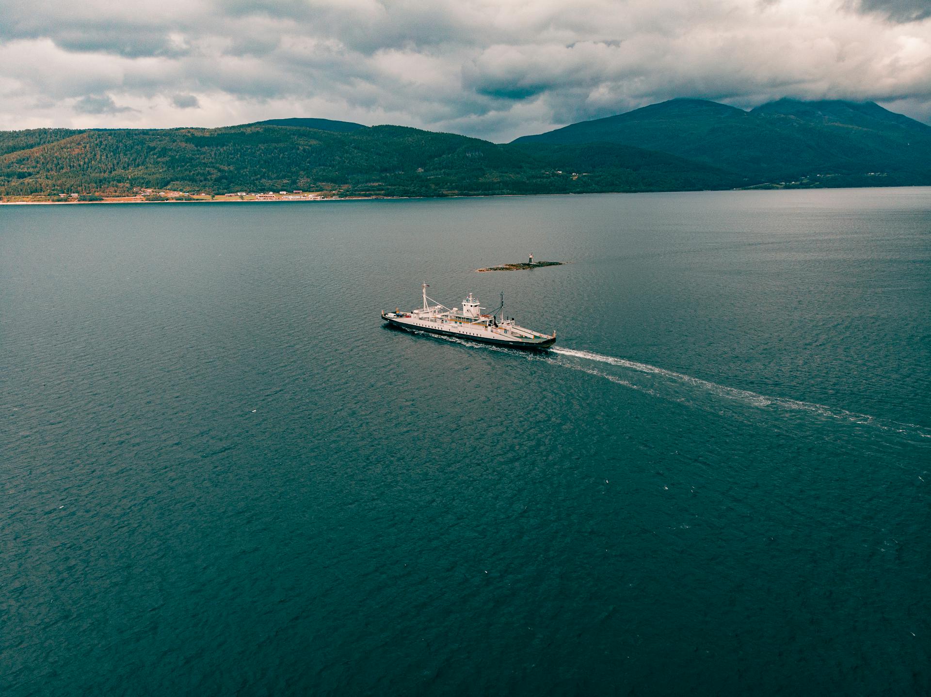 A ferry cruises through the serene waters of a Norwegian fjord under a cloudy sky.