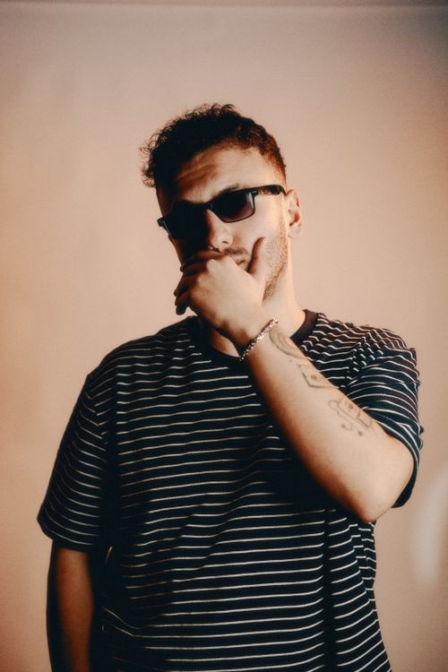 Free Young man in striped T-shirt and sunglasses posing thoughtfully in studio setting. Stock Photo