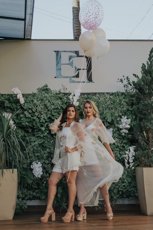 Photo of Two Women Posing in Front of Green Leafed Hedge Wall