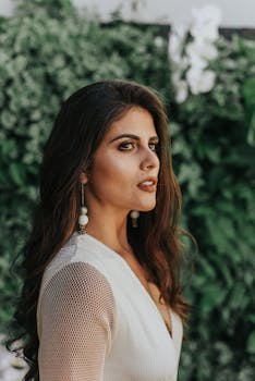 黑发女子侧身立于郁郁葱葱的绿叶前，姿态优雅