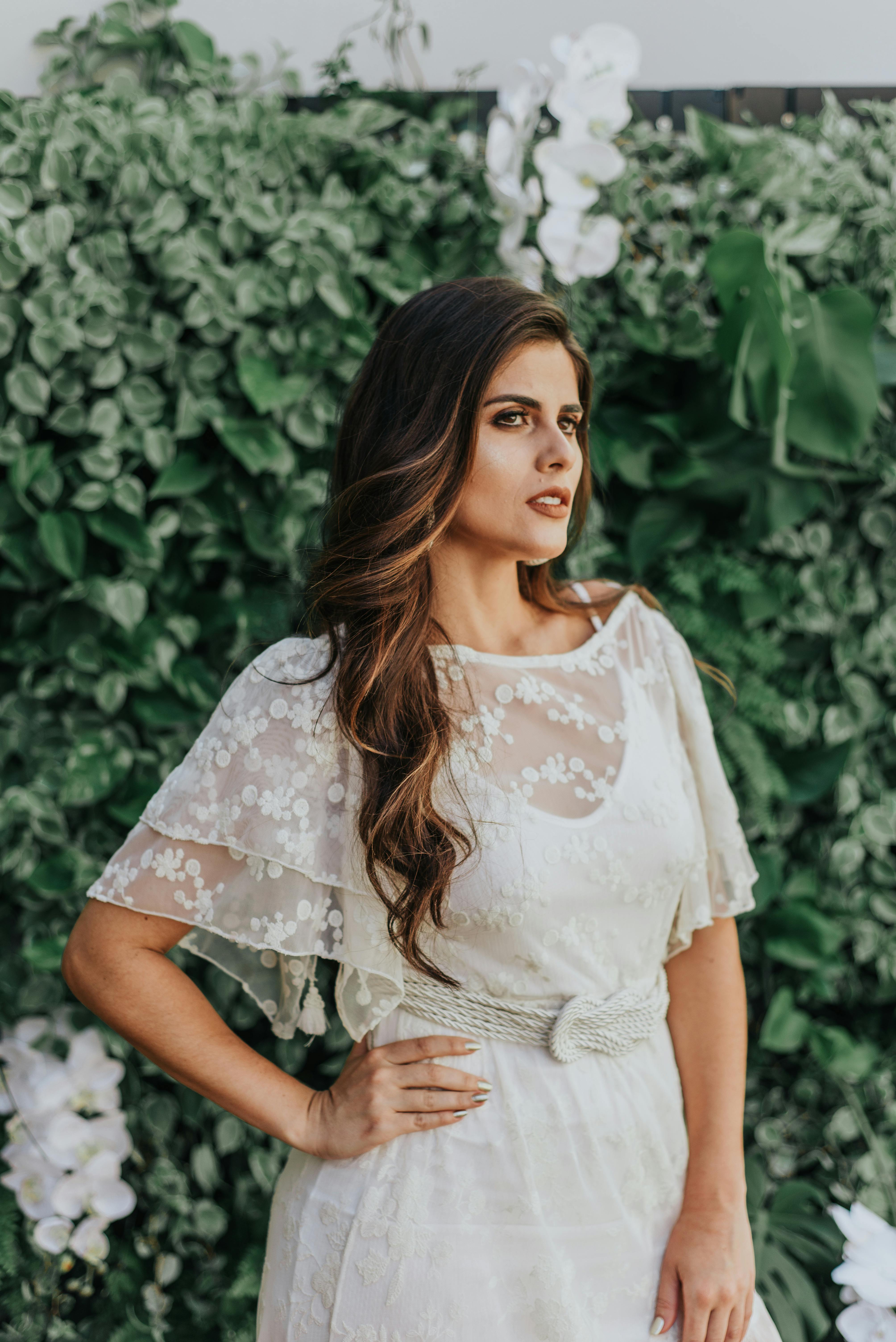 在宁静的户外环境中，一位身着时尚白色连衣裙的女子在郁郁葱葱的绿色背景下摆姿势