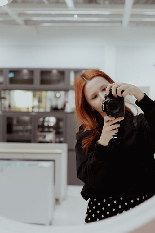 Free Redhead woman capturing a photo using a DSLR camera indoors. Stock Photo