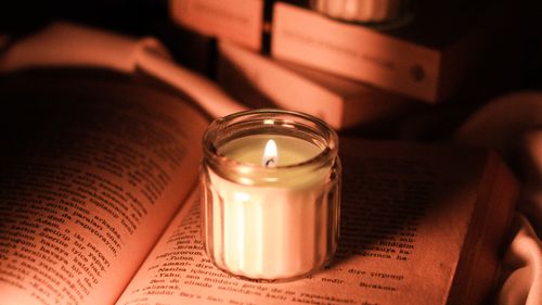 Free A glass candle softly lights up the pages of an open book, creating a serene and cozy reading atmosphere. Stock Photo