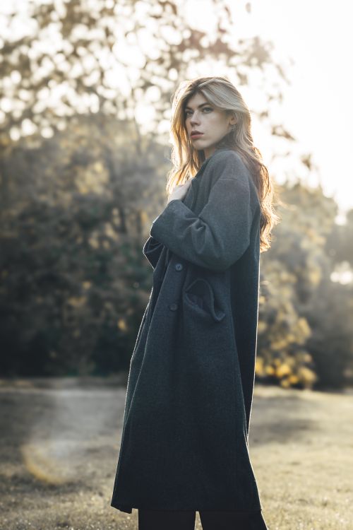 Free Blonde woman in stylish coat posing in a sunny park during fall, showcasing fashion photography. Stock Photo