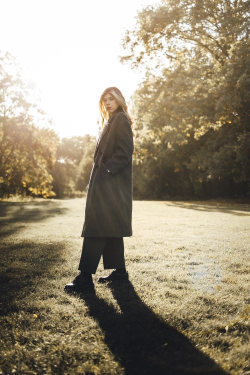 Free A woman in fashionable attire poses in a sunlit park during fall, blending elegance and nature. Stock Photo