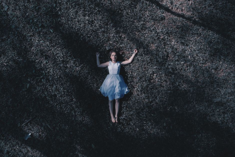 A woman in a white dress lying gracefully on grass, captured from above, evoking tranquility.