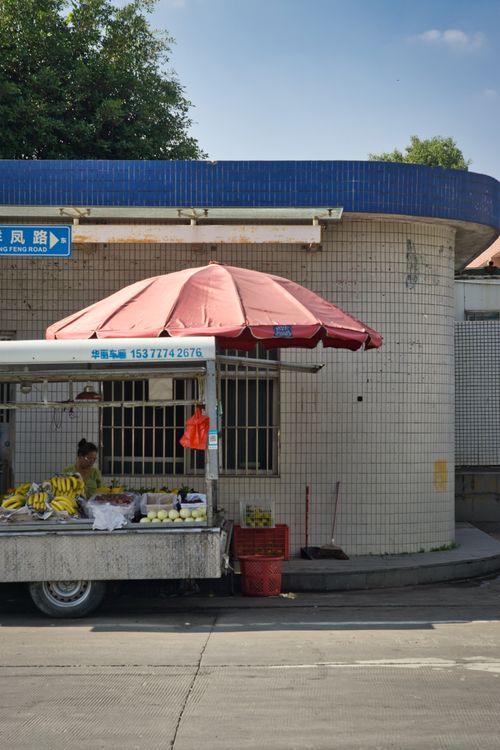 Free Street market stall selling fruits under a red umbrella against a building facade. Stock Photo