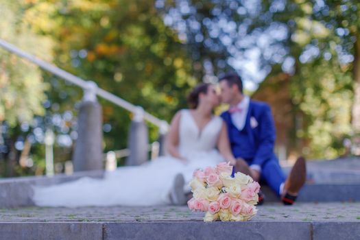 A bride and groom share a romantic moment outdoors with a bouquet in the foreground.