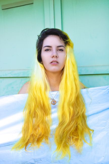 Young woman with bright yellow hair against a pastel green backdrop.