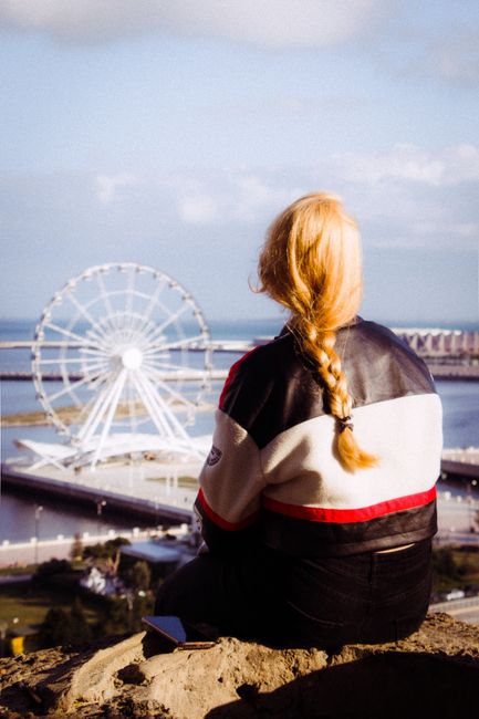 Blonde woman gazes at a seaside Ferris wheel, capturing a serene moment of leisure.