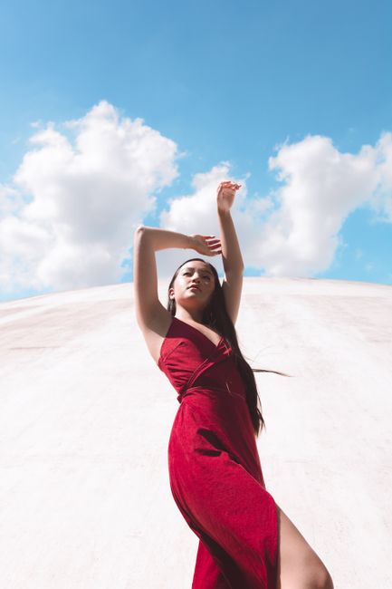 A graceful woman in a vivid red dress poses against a bright blue summer sky.