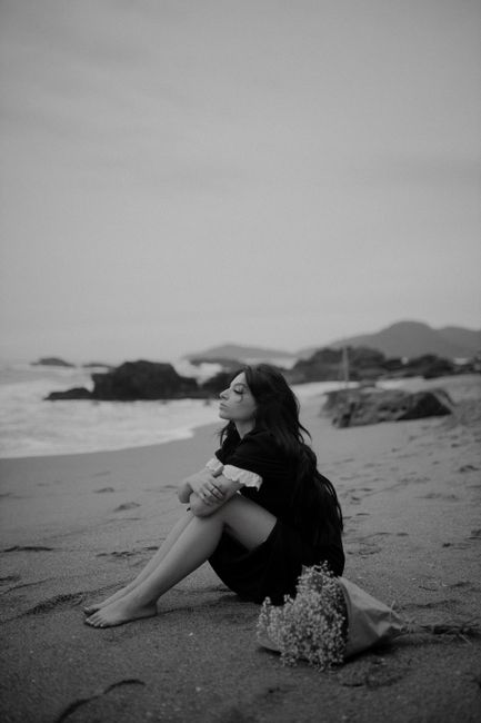 A thoughtful woman sits on a serene beach, embracing nature's tranquility. Black and white photography.