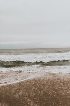 A serene view of the ocean waves gently caressing the sandy beach under a cloudy sky.