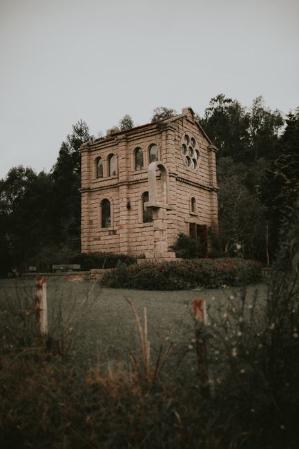 Fotomural Hermosa capilla de piedra rodeada de vegetación exuberante y árboles en un entorno al aire libre.