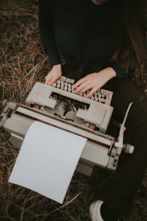 woman sitting outdoors typing on vintage typewriter