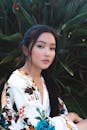 一位年轻女子身着花卉服装，在郁郁葱葱的绿色植物映衬下，显得格外优雅