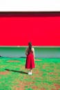 一名身穿红色连衣裙的女子站在绿地上，面对着一面鲜艳的红墙，形成了鲜明的对比