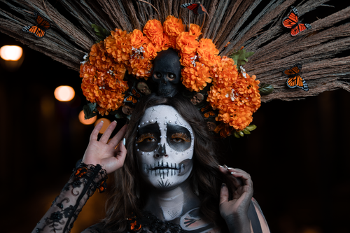 Free Elegant Catrina with skull face paint and orange flower headpiece in Morelia, México. Stock Photo