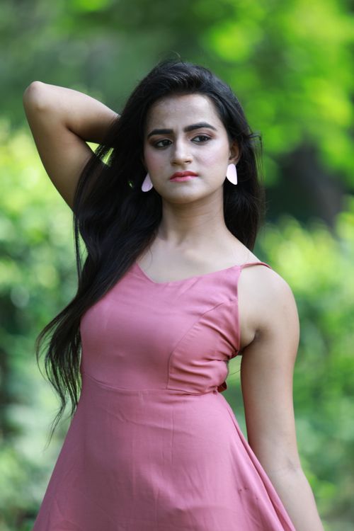 Free Stunning portrait of a woman in a pink dress posing in a lush, green outdoor setting. Stock Photo
