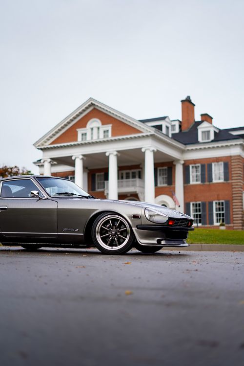 Free Vintage Datsun 240Z sports car parked in front of a grand mansion on a cloudy day. Stock Photo