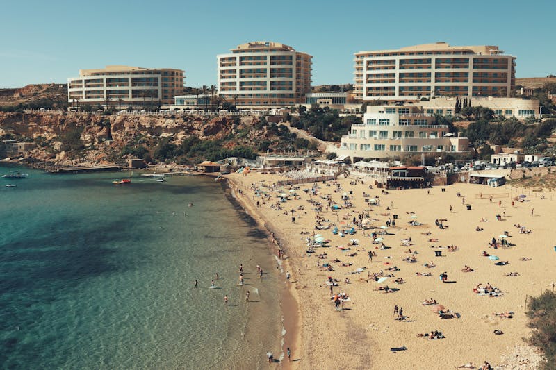 People relaxing on golden sand at Golden Bay beach in Mellieħa Malta with turquoise Mediterranean water