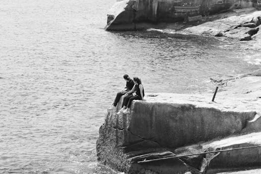 A couple sits on a rocky seaside cliff, soaking in the serene ocean view in Valletta, Malta.