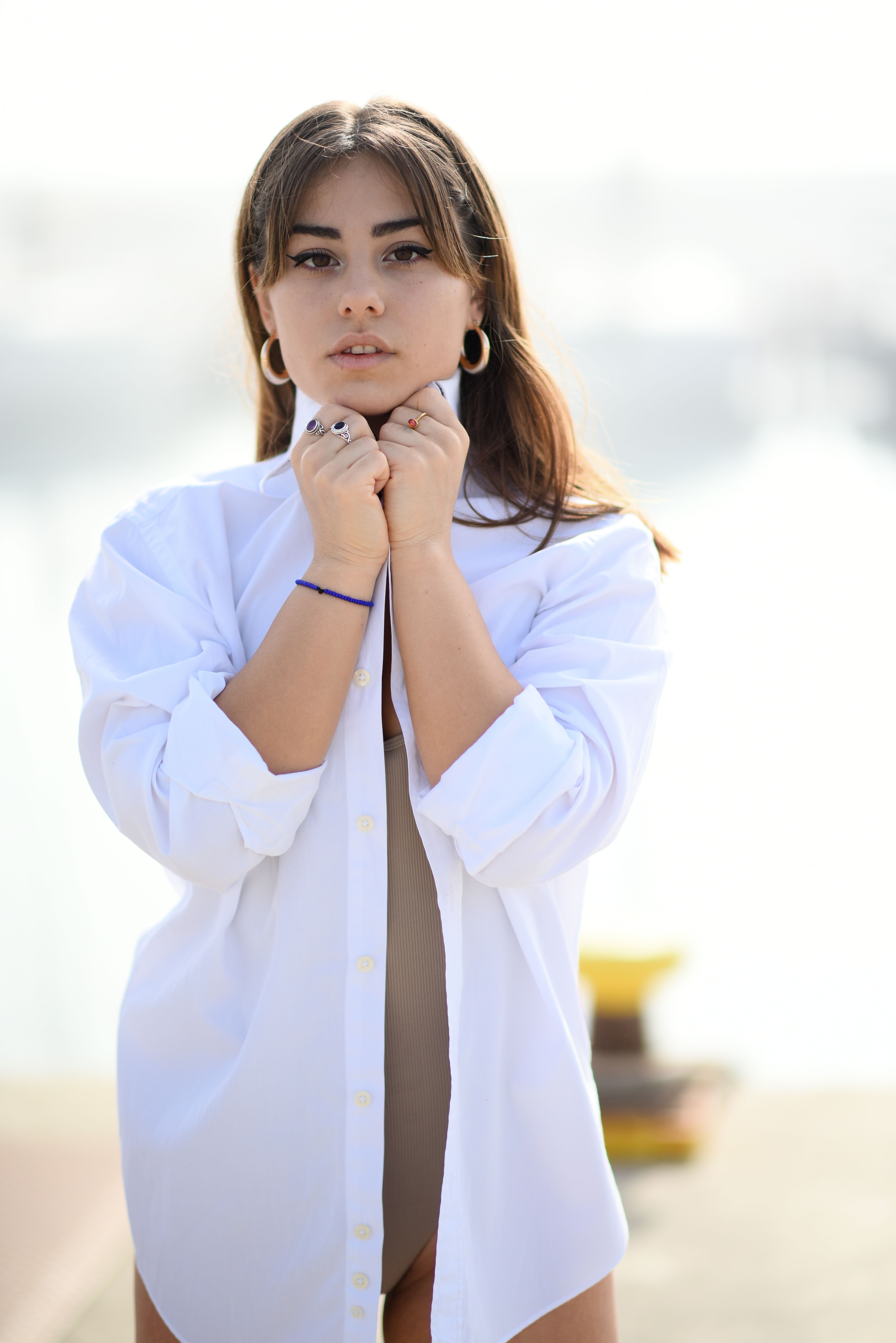 A young woman poses confidently outdoors in a fashionable white shirt, exuding elegance.