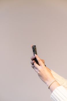 Close-up of hands holding a smartphone against a beige background, showcasing mobile interaction.