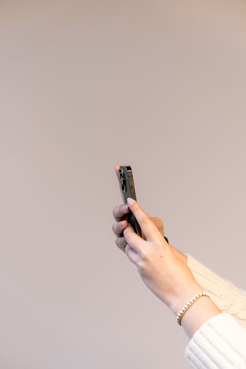 Free Close-up of hands holding a smartphone against a beige background, showcasing mobile interaction. Stock Photo