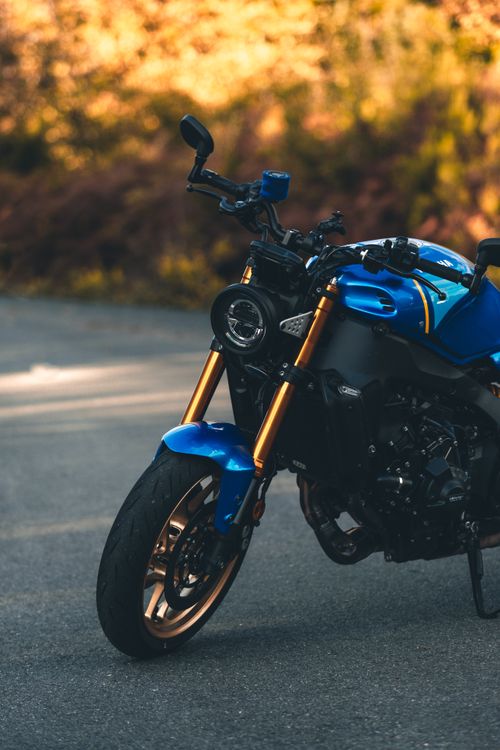 Free Close-up of a blue motorcycle on a road with autumn leaves in the background. Stock Photo