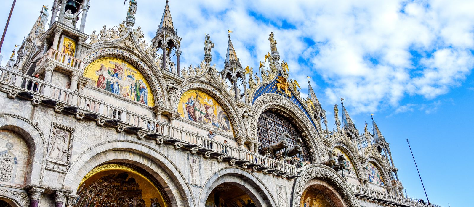 Low angle view of the ornate facade of St. Mark's Basilica under a blue sky in Venice, Italy.
