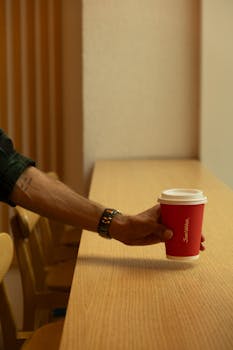 A man holding a red take-out cup in a cafe, showcasing minimalist interior design.
