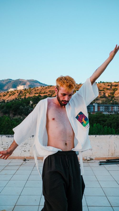 Free Young man with a beard dances freely on a terrace, showcasing a fun and carefree moment Stock Photo
