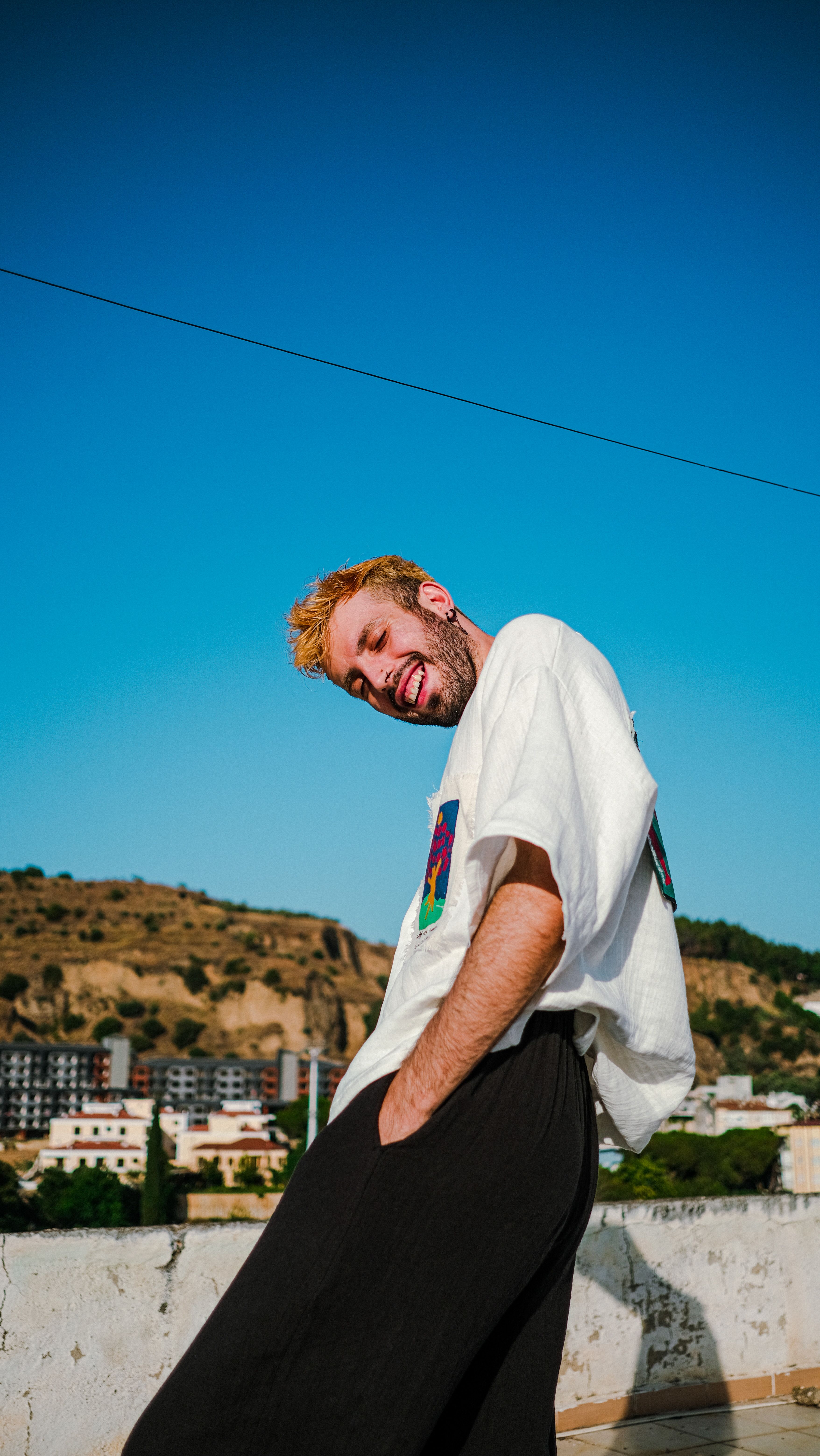 Happy young man with dyed hair smiling outdoors against a blue sky and landscape.