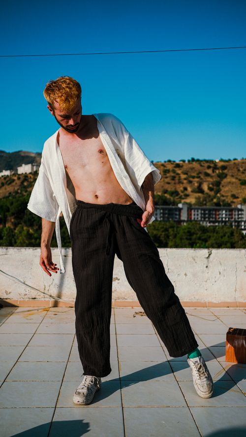 Free A young man in black pants and white shirt poses stylishly on a sunny rooftop. Stock Photo