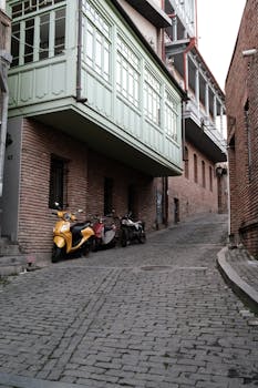 Discover a quaint cobblestone street in Tbilisi, Georgia featuring historic architecture and parked motorcycles.