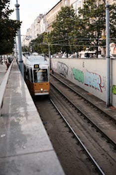 A tram travels down a vibrant street with historic buildings and graffiti art in Budapest.