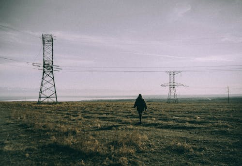 Woman Walking in the Field with a View of Transmission Towers 