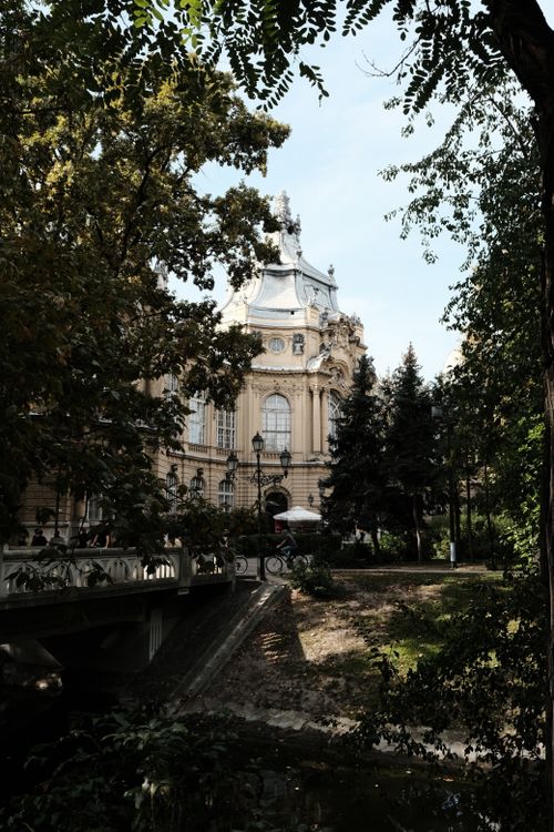 Free Serene view of a historic Budapest building, framed by lush trees in a garden setting. Stock Photo
