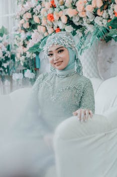 Smiling bride in turquoise traditional attire amidst floral decorations at a wedding ceremony.