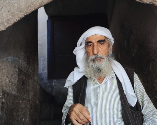 Free An elderly man with a turban and gray beard standing by stone walls. Stock Photo