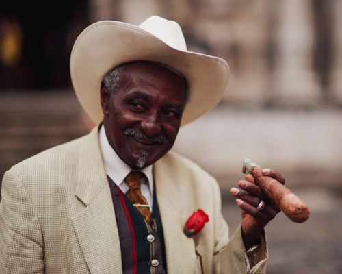 Free A senior man in a white hat and suit smiling while holding a cigar. Stock Photo