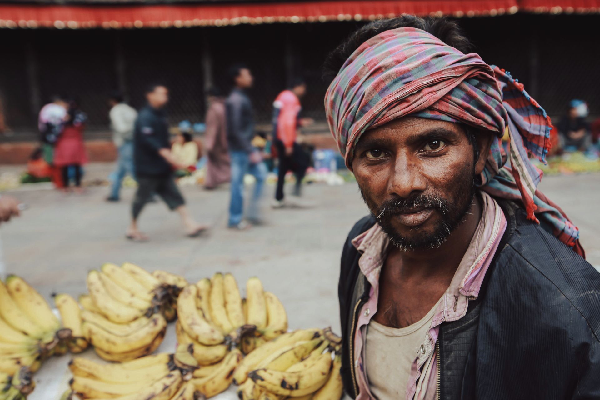 A hardworking vendor selling bananas in a busy marketplace with a traditional headscarf and determined look.